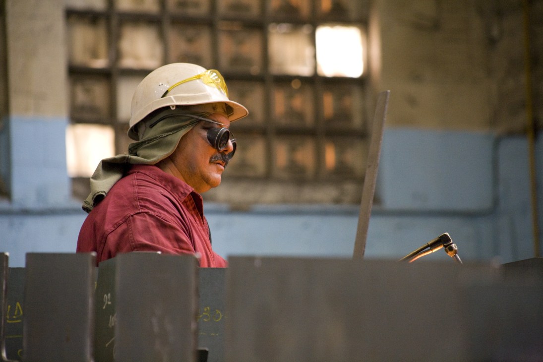 A welder wearing a white hard hat and protective gear works at Navantia shipyard.