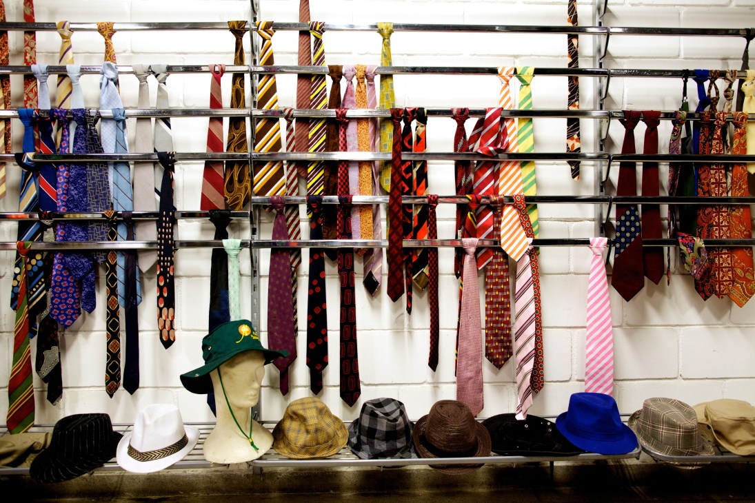 Metal rack displaying dozens of colorful neckties and hats on shelf below for costume storage at Globo television studio.