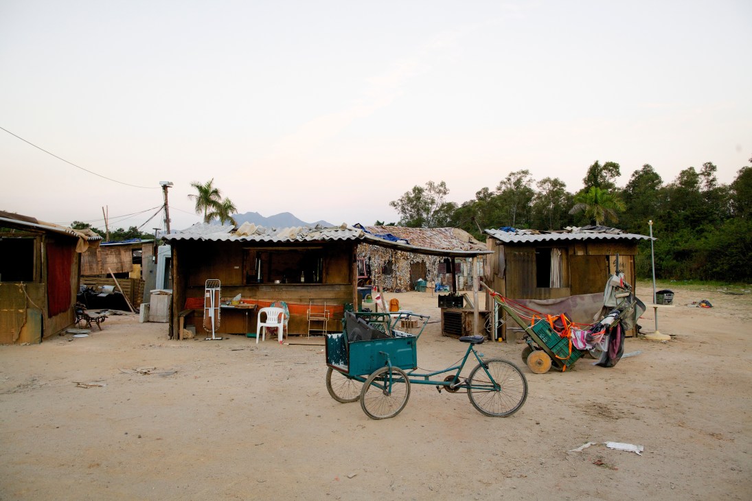 A constructed favela set with makeshift houses, bicycles, and props on sandy ground at Globo's Projac studio lot.