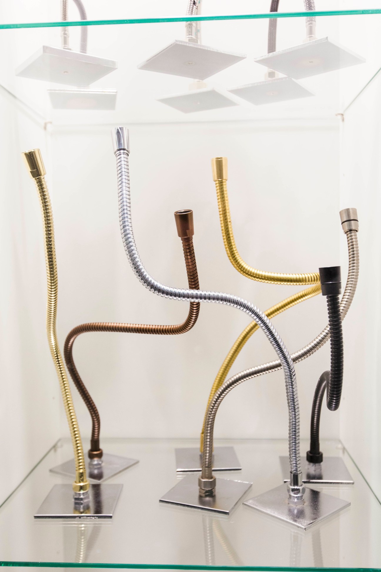 Display of flexible metal shower hoses in various finishes including gold, silver, brown and black on stands.