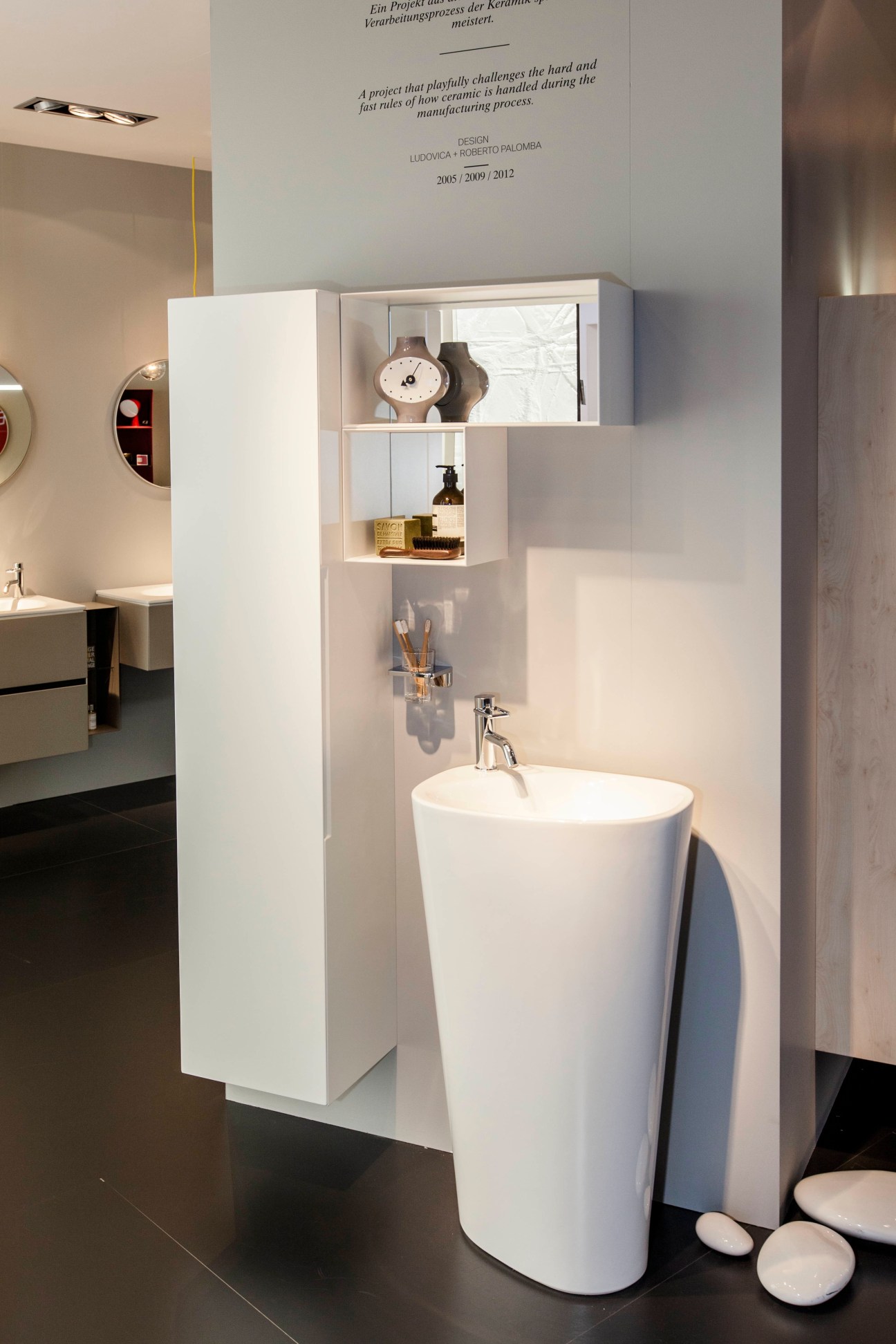Laufen's minimalist bathroom display with white pedestal sink, wall-mounted storage, and modern fixtures.