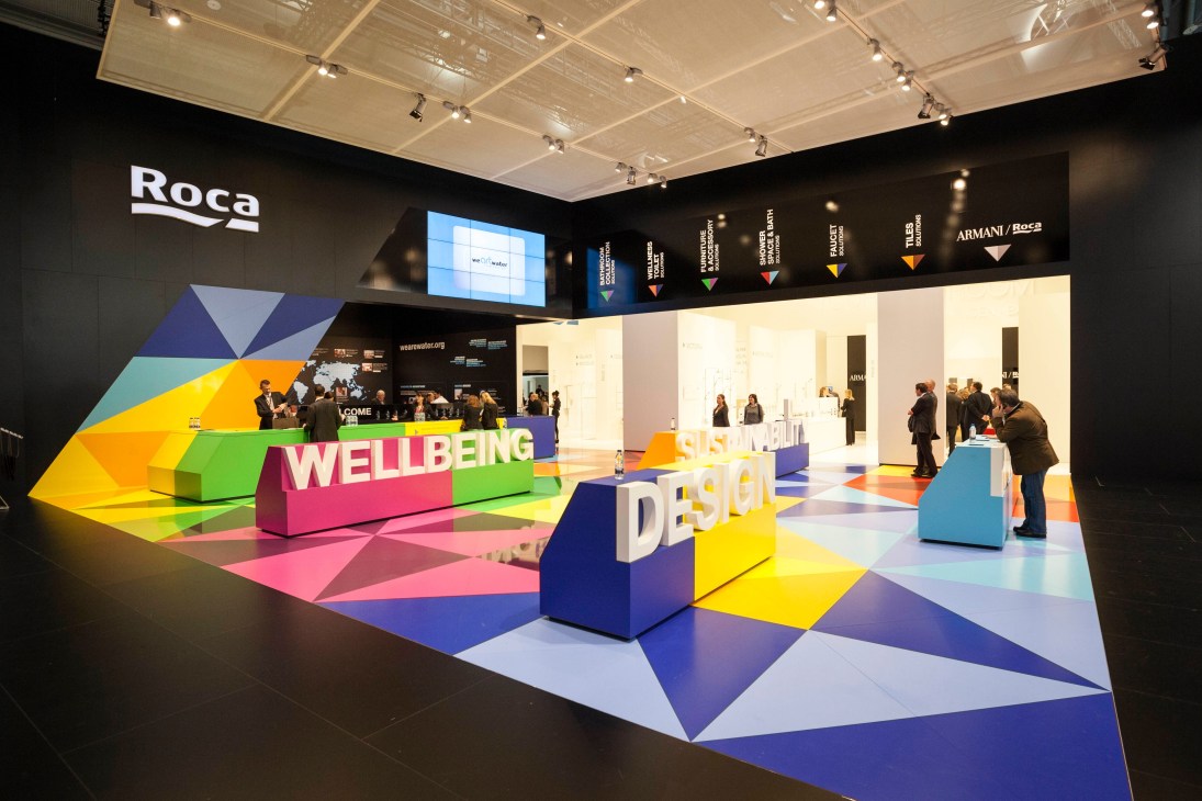 Roca's colorful exhibition booth at ISH trade fair with geometric floor patterns and 'Wellbeing Design' signage.
