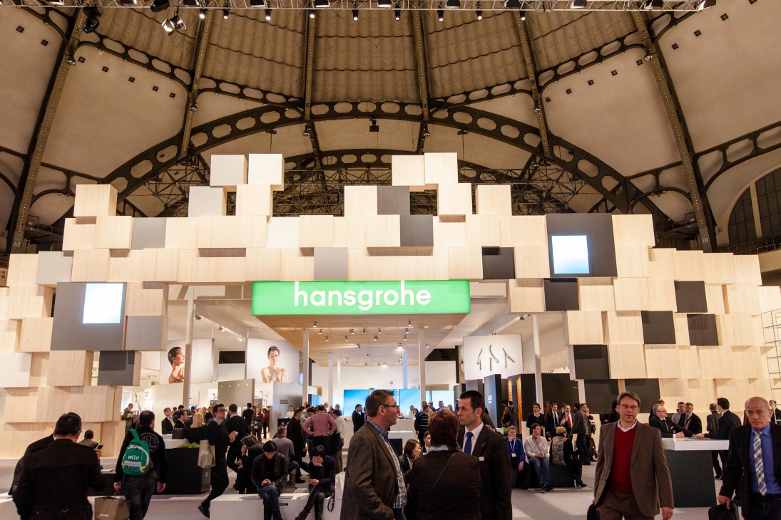 Hansgrohe's trade fair booth with geometric wooden facade and green signage at ISH Frankfurt.