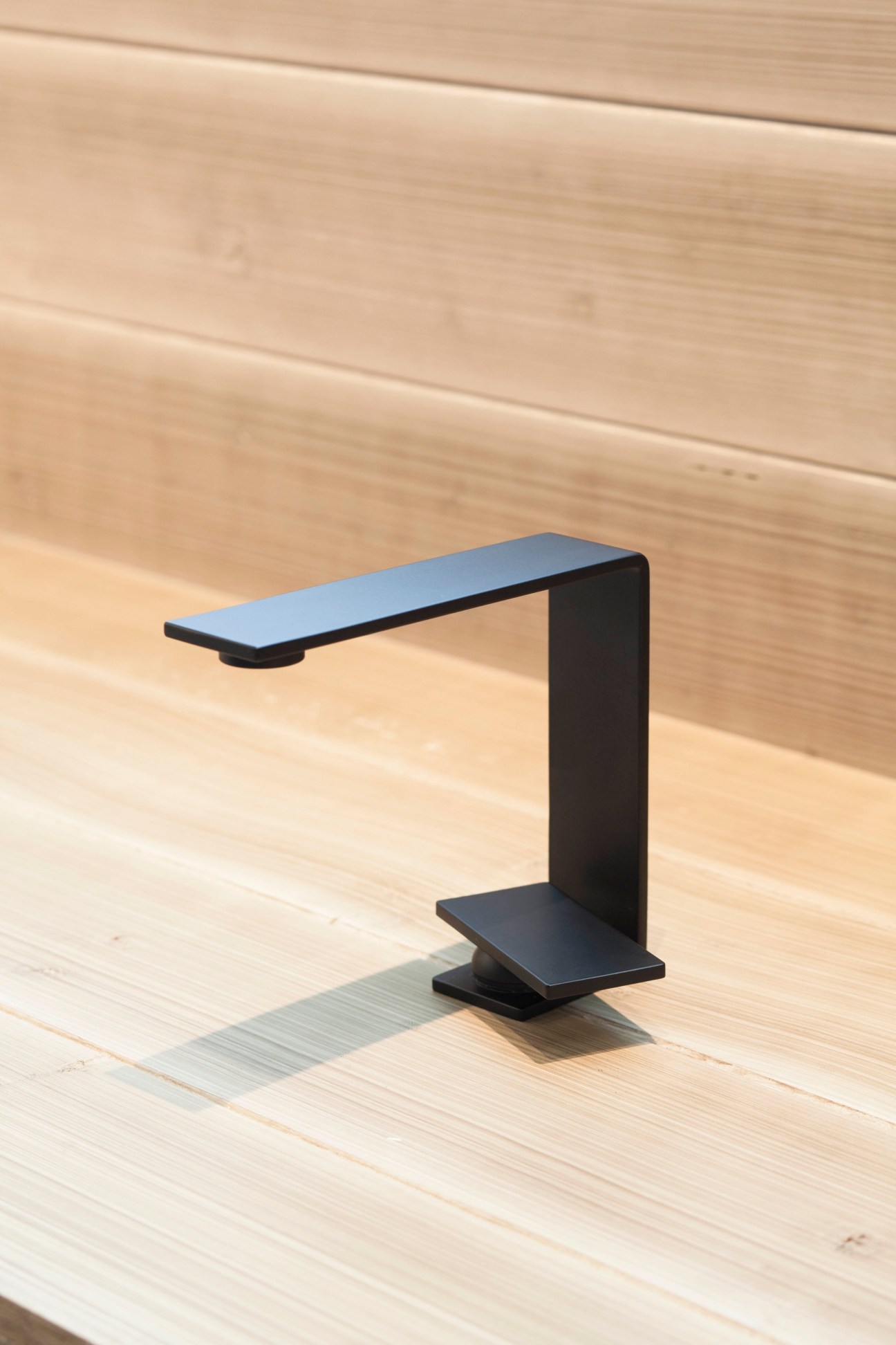 Modern black minimalist tap with angular design displayed on wooden surface.