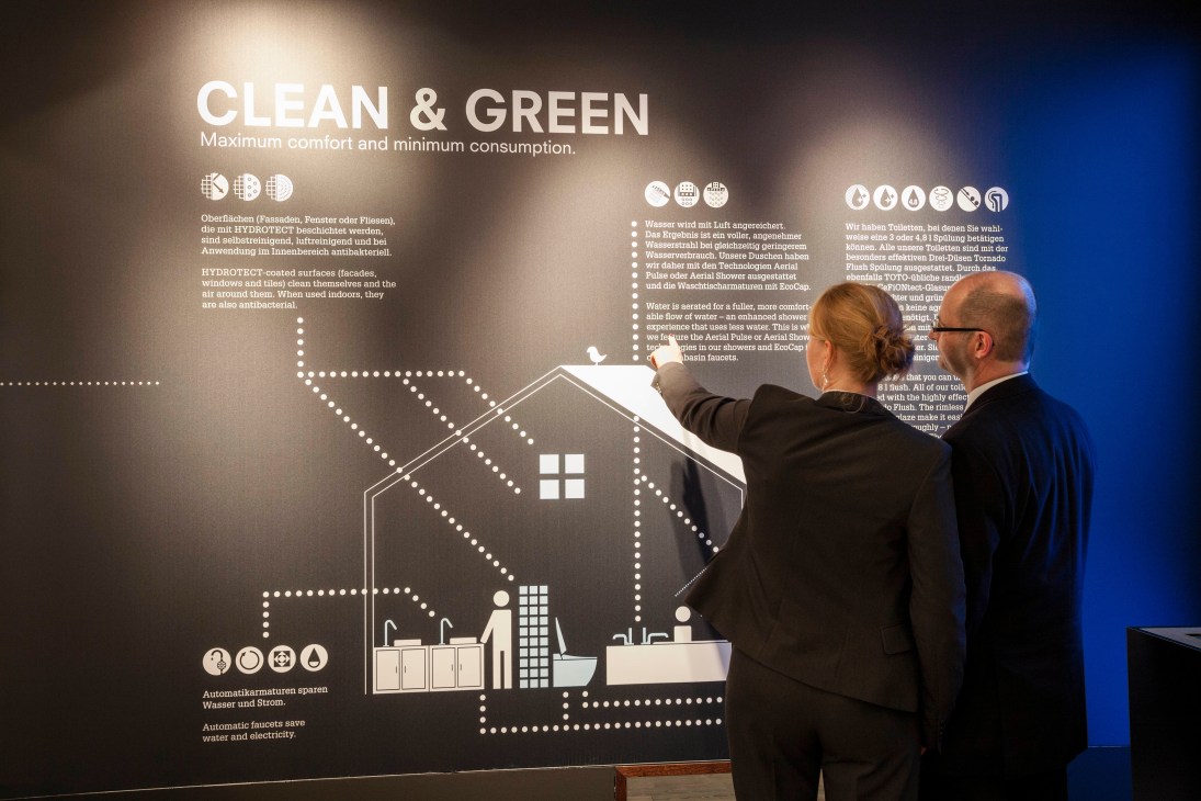 Two men in business attire examine an illuminated interactive display about sustainable sanitation solutions at ISH 2013.