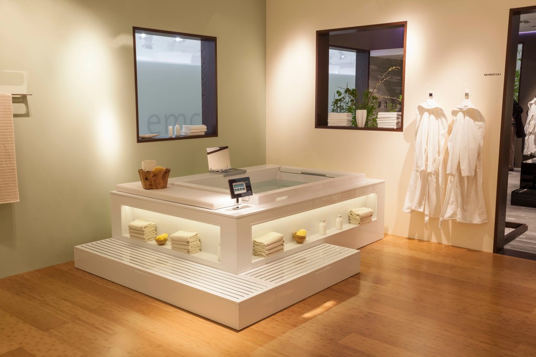 TOTO's minimalist bathroom display booth with a sunken rectangular bathtub and white towels.