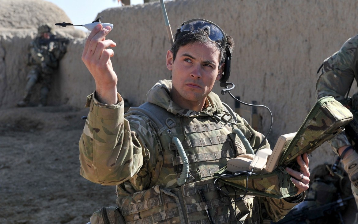 Soldier in tactical gear holding a small Black Hornet nano-UAV drone in an Afghan desert setting.