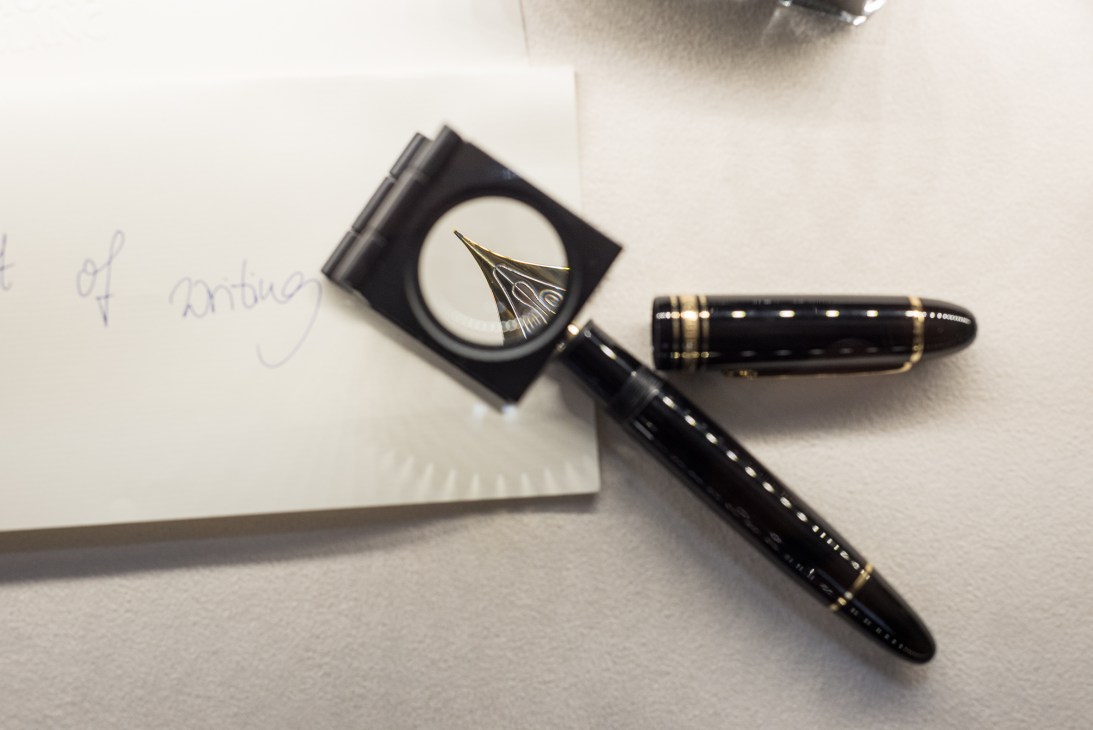Montblanc fountain pen with 18-carat gold nib displayed next to magnifying glass and handwritten paper.