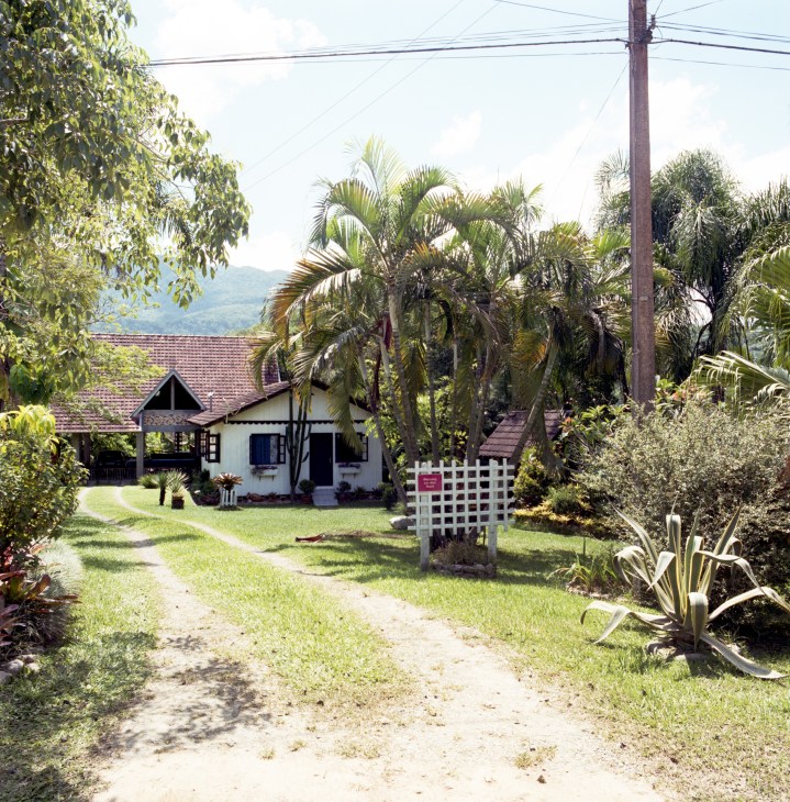 Traditional half-timbered Pomeranian house with pitched roof surrounded by tropical palm trees and lush vegetation in Brazil.