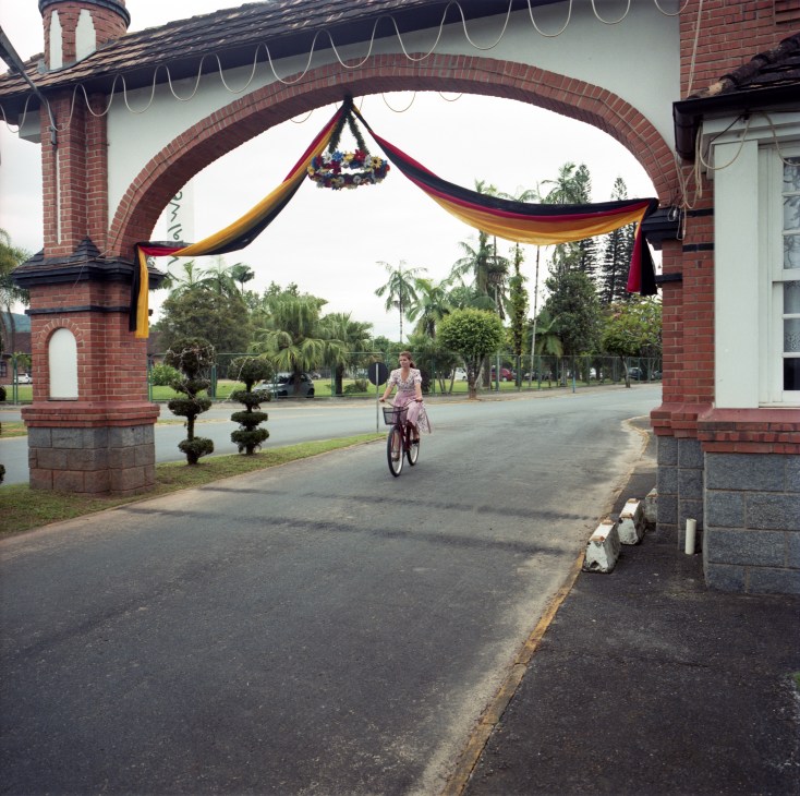 A woman rides a bicycle through a brick archway decorated with German flag ribbons in Pomerode, Brazil.
