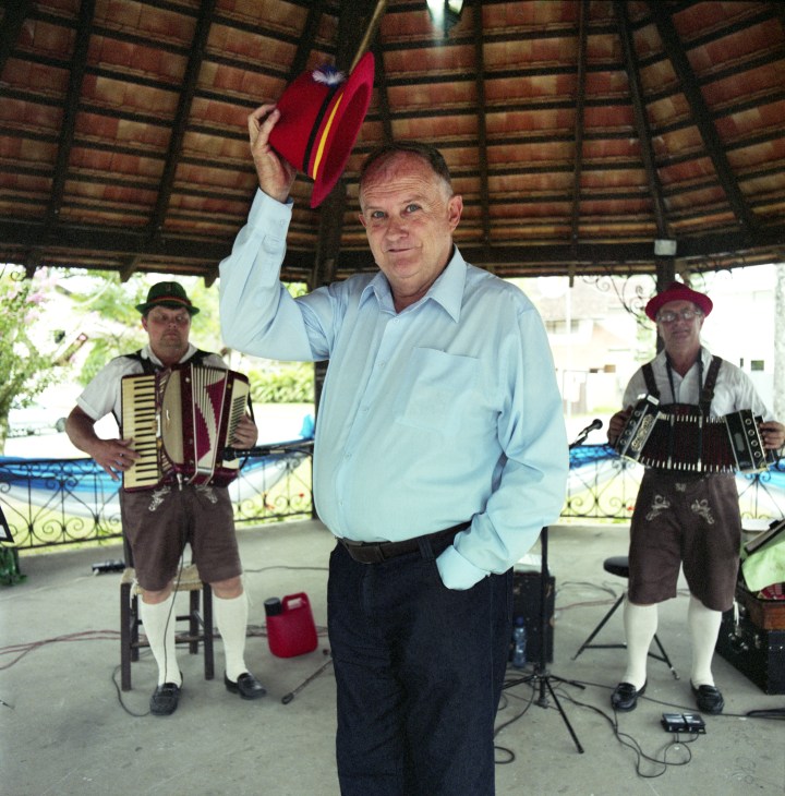 Fred Ullrich, secretary for tourism, holds a red hat while standing with accordion players at a festival event in Pomerode.