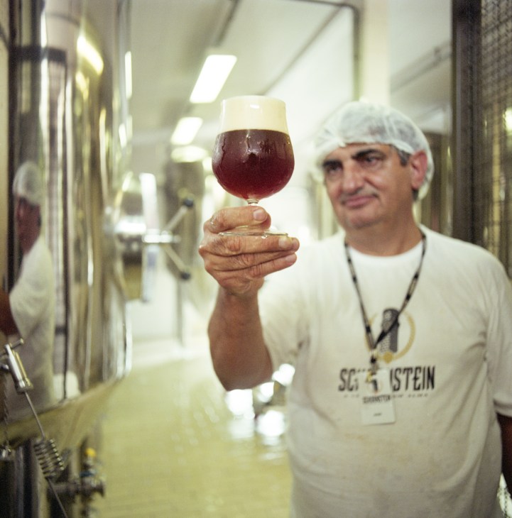 Master brewer José Carlos da Silva Rosa holds a glass of dark beer in a brewery facility.