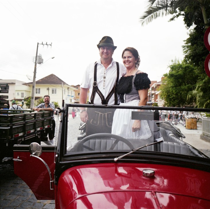 Mayor Rolf Nicolodelli in lederhosen and a woman in traditional German dress ride in a red convertible at the Festa Pomerana parade.