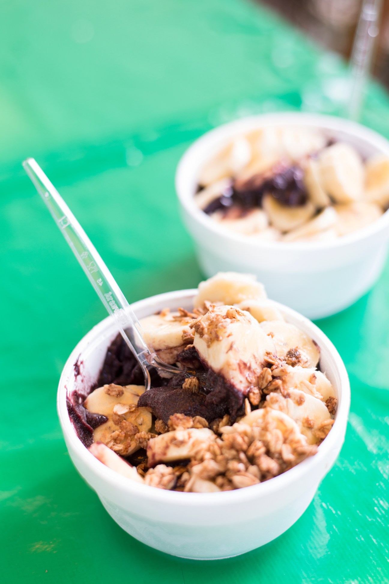 Bowls of ice cream with granola and toppings on a bright green surface.