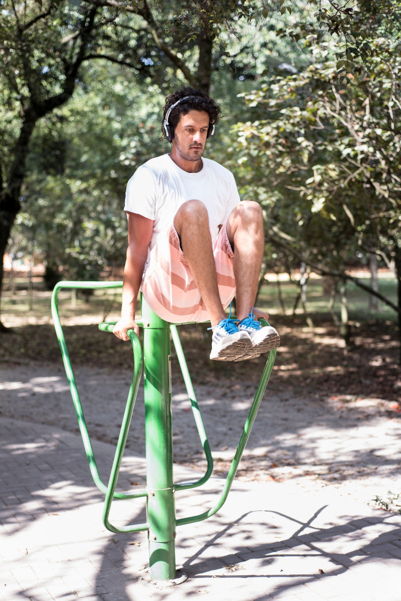 Man exercising on outdoor fitness equipment in a tree-lined park setting.