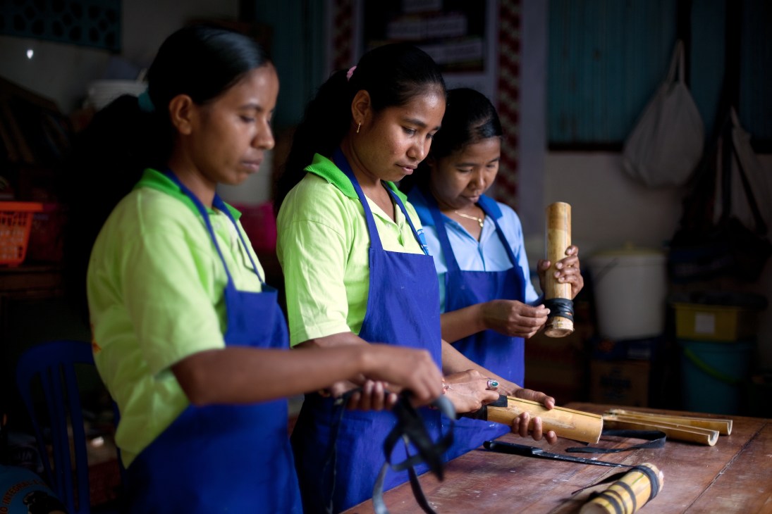 Women in blue aprons working with wooden tools at a craft workshop table.