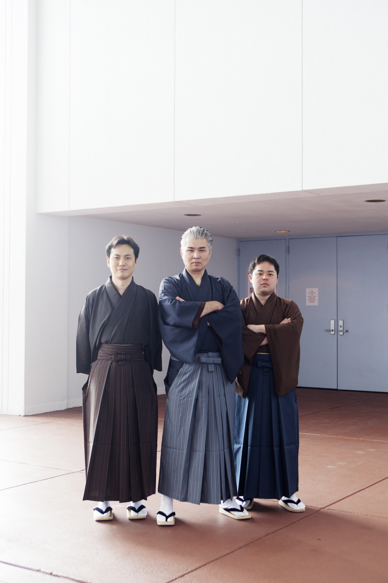 Three men wearing traditional Japanese kimonos standing in a modern convention center hall.