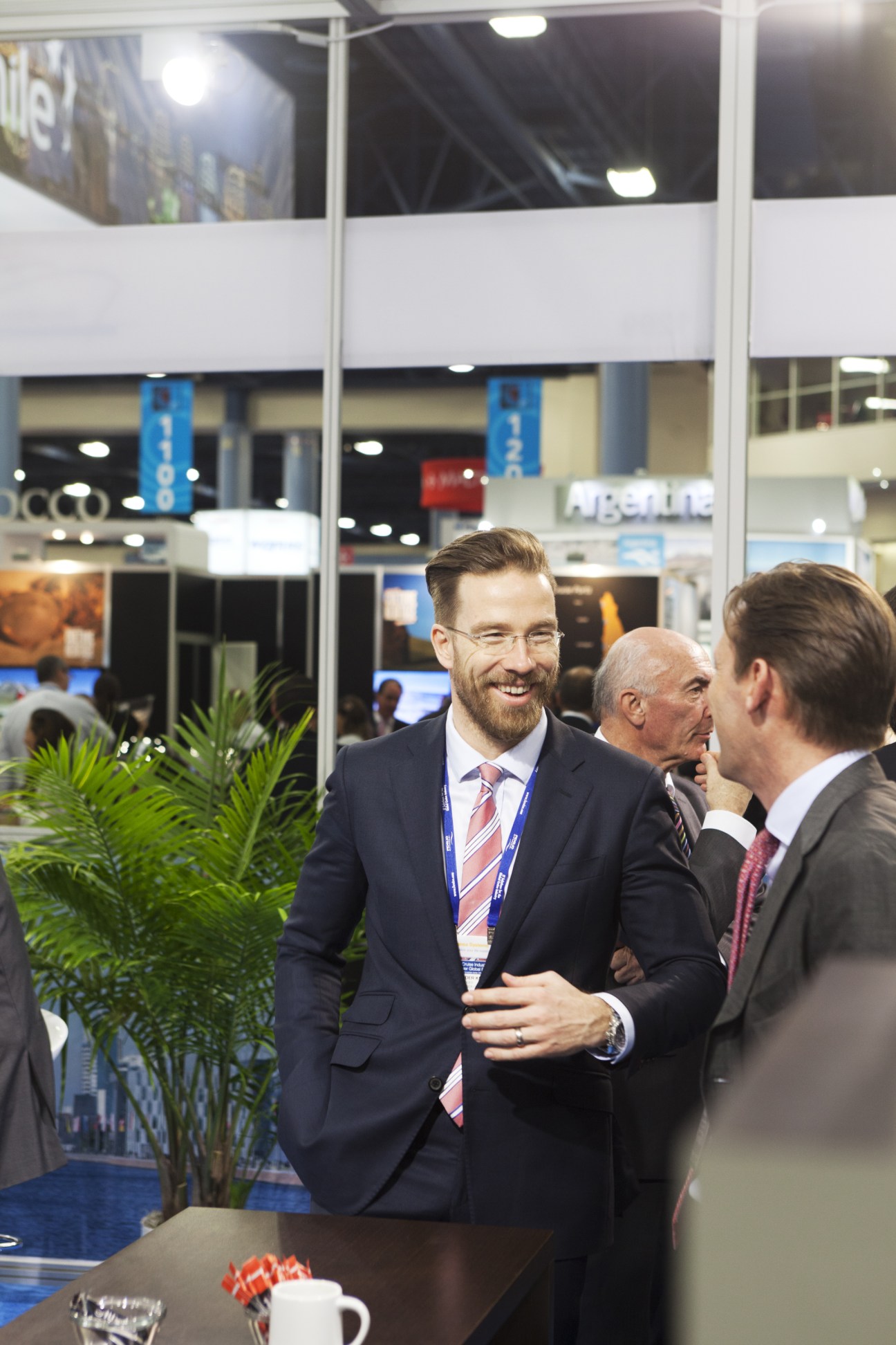 Business professionals in suits networking and conversing at a cruise industry conference exhibition hall.