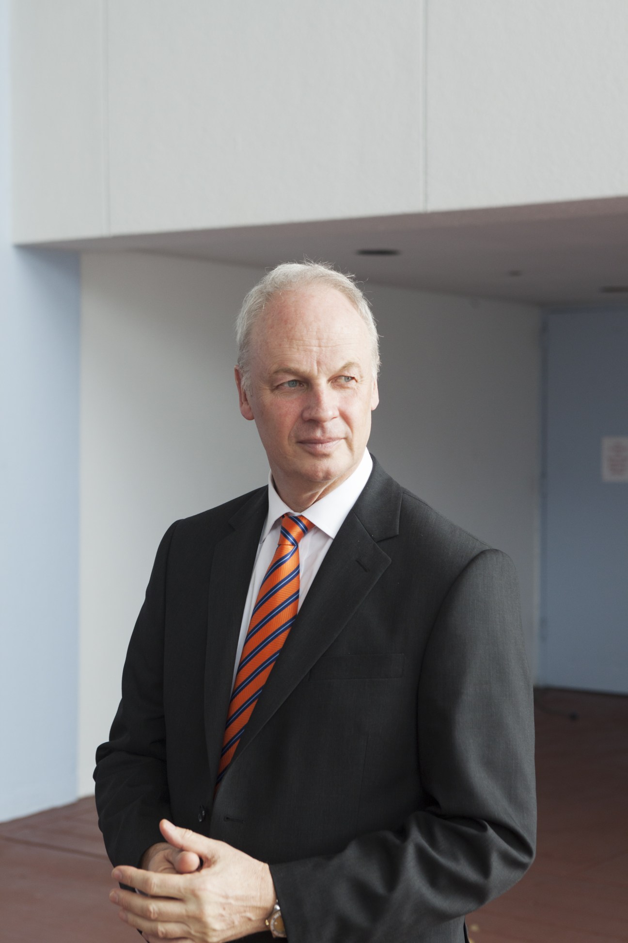 World Travel & Tourism Council president David Scowsill standing in a modern interior wearing a dark suit and orange striped tie.