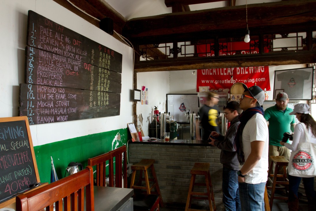 Interior of Great Leap Brewery in Beijing with beer menu on chalkboard and customers at counter.