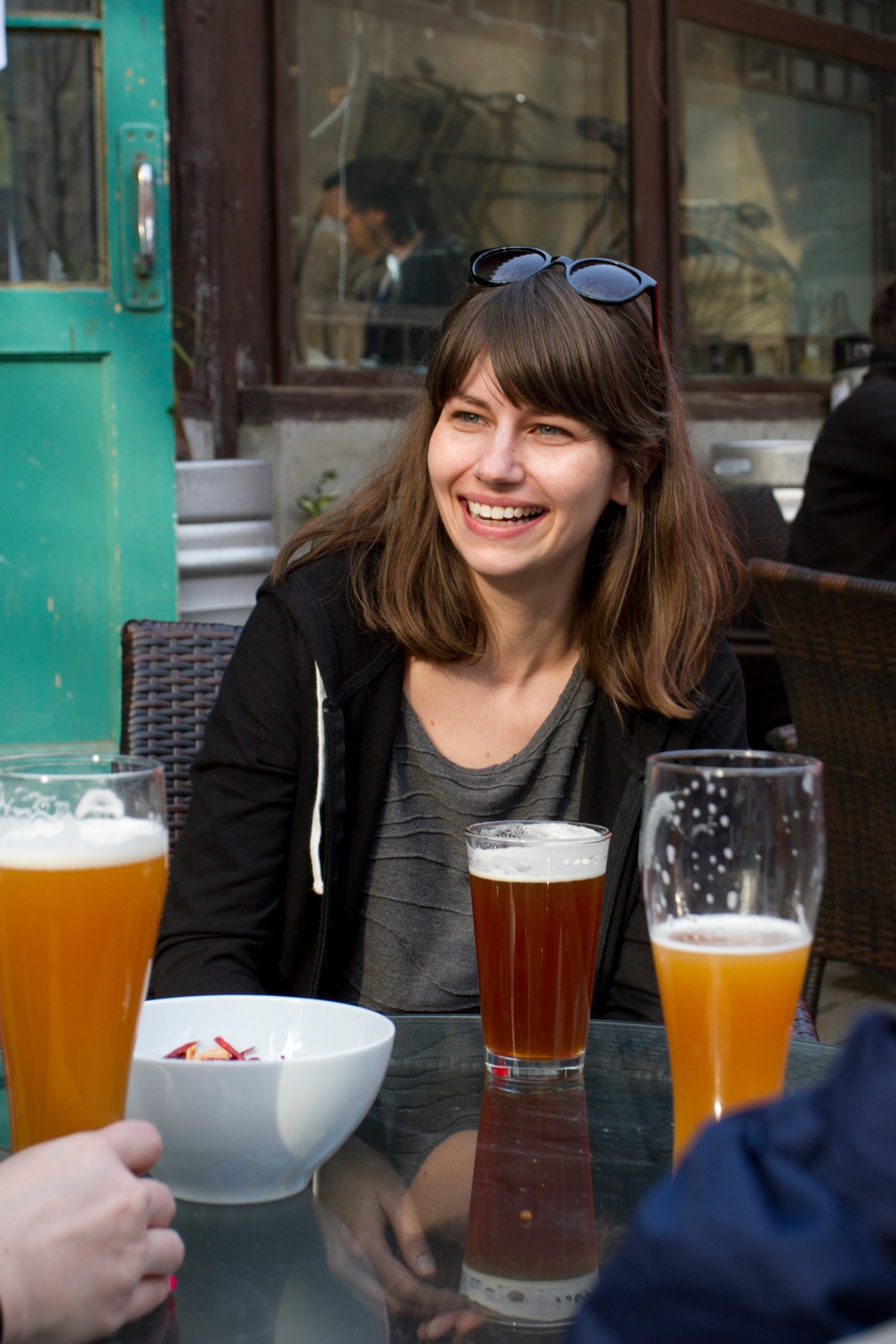 Woman smiling at outdoor table with beer glasses and turquoise storefront behind