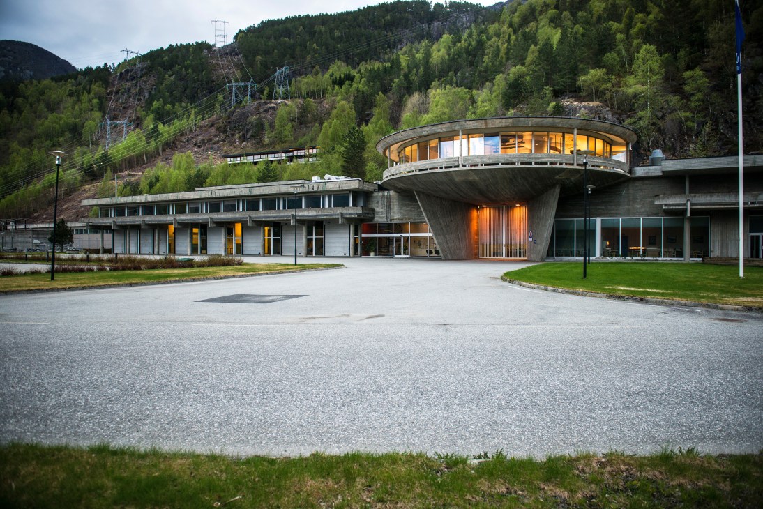 Modern concrete hotel building with curved design nestled in forested mountainous landscape.
