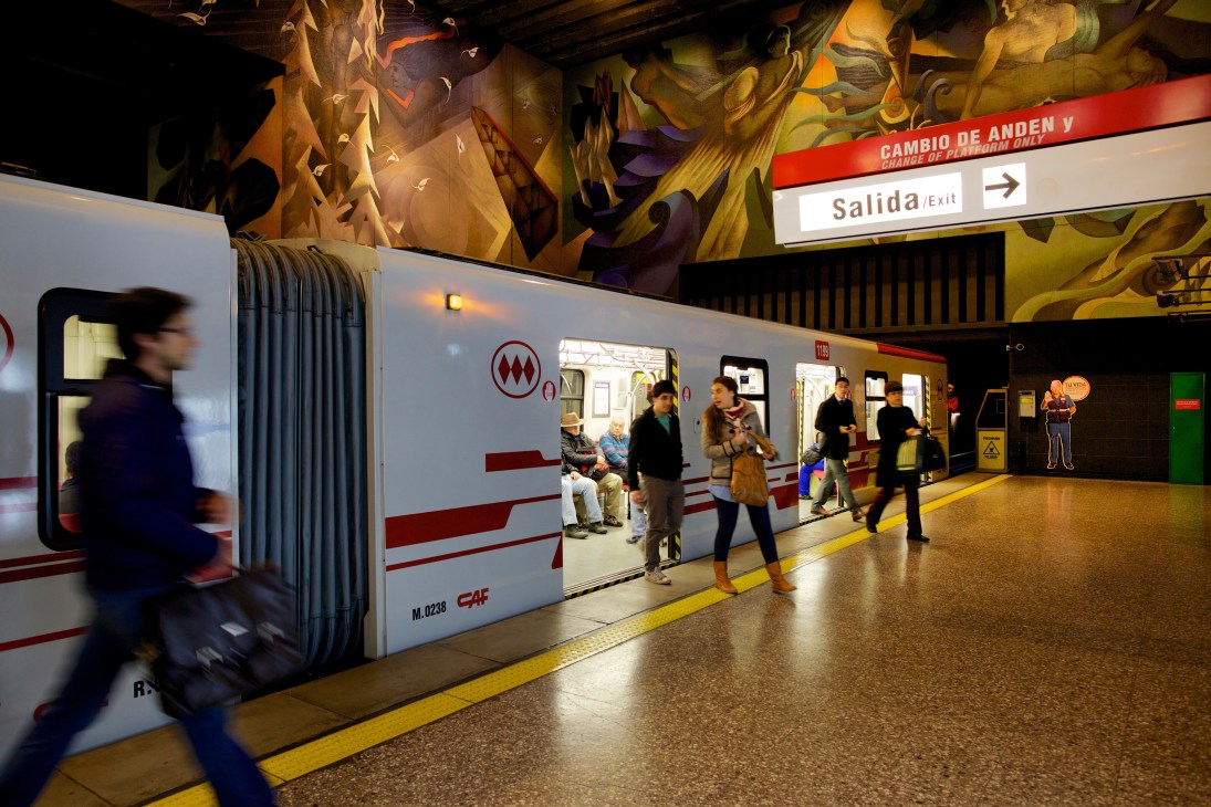 Passengers boarding a white metro train with red stripes at Universidad de Chile subway station in Santiago