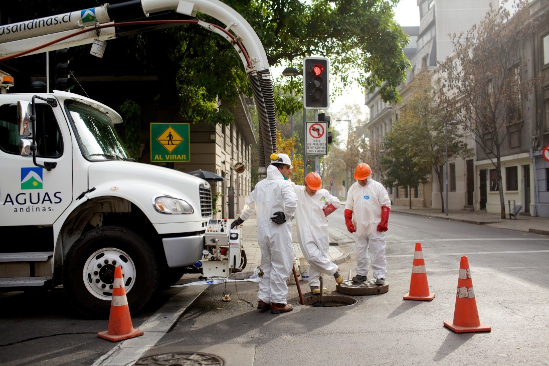 Aguas Andinas maintenance crew in white protective suits working on a street in Santiago