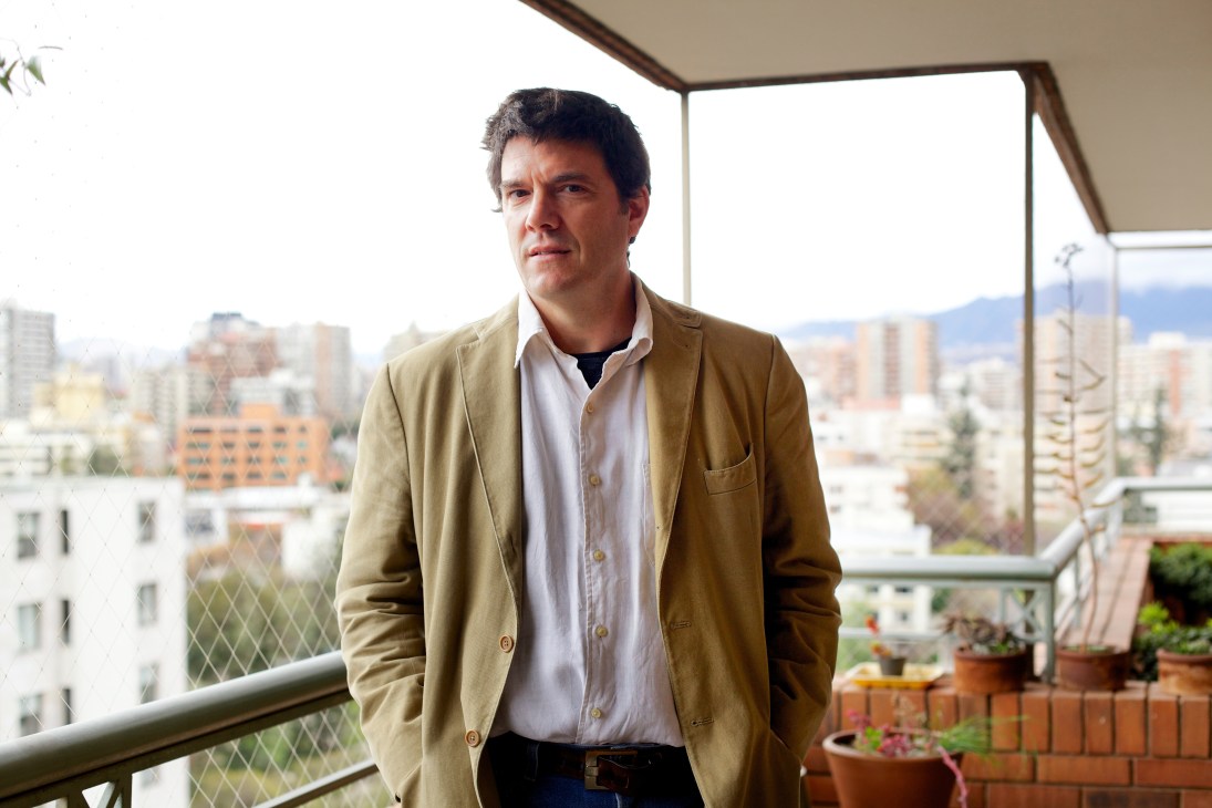 Professor Andrés Gómez-Lobo standing on a balcony overlooking Santiago with the city skyline in the background.
