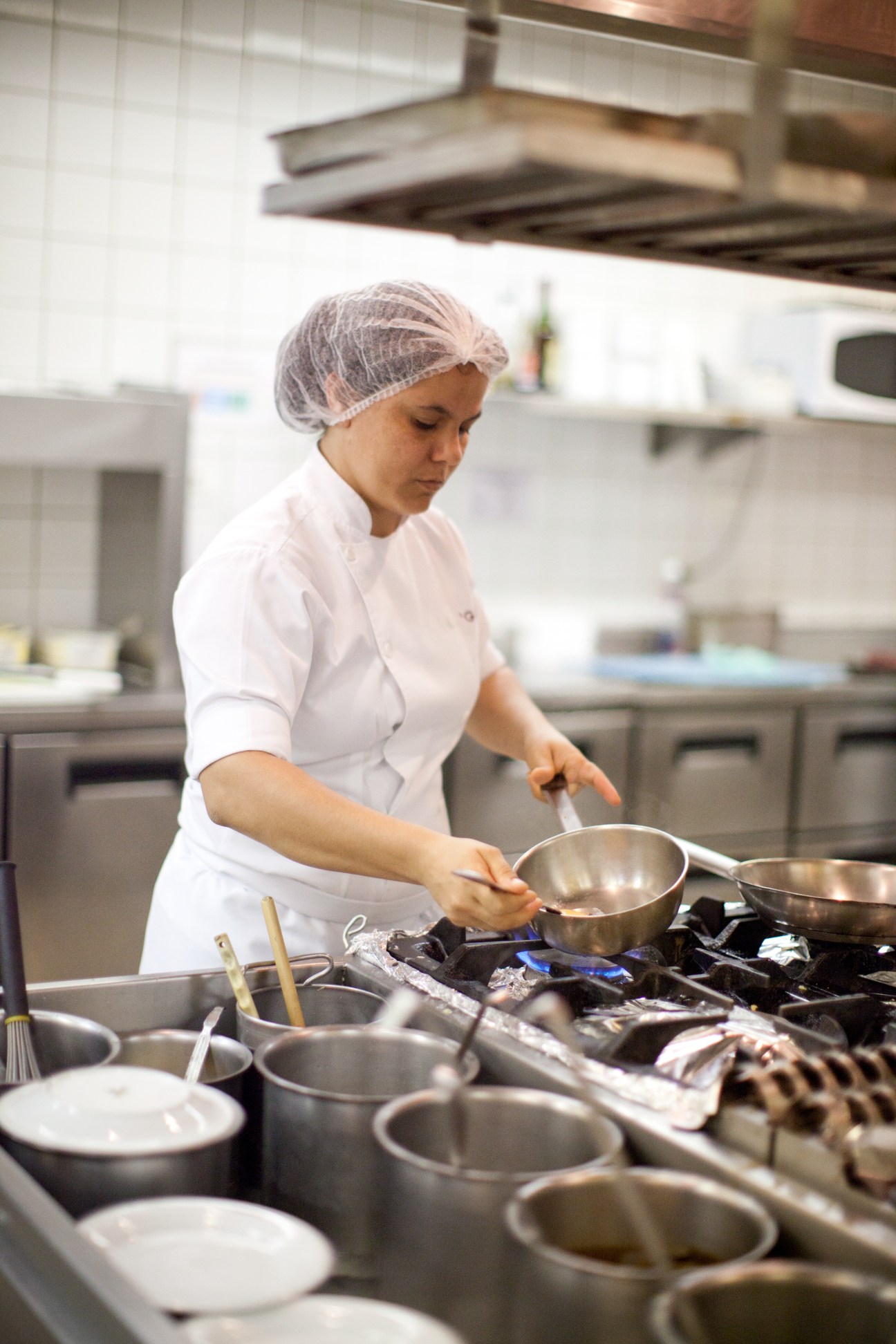 Chef in white uniform and hairnet preparing food at Gero's kitchen stove.