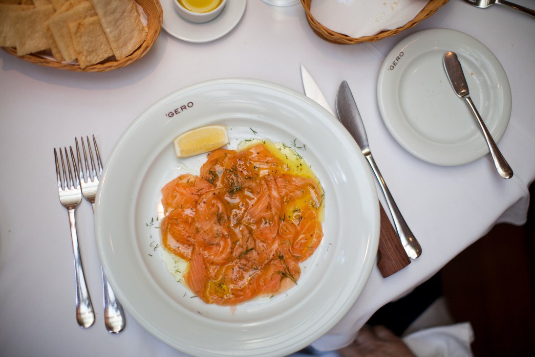 Salmon carpaccio with lemon and olive oil served at Gero restaurant on a white plate with cutlery.