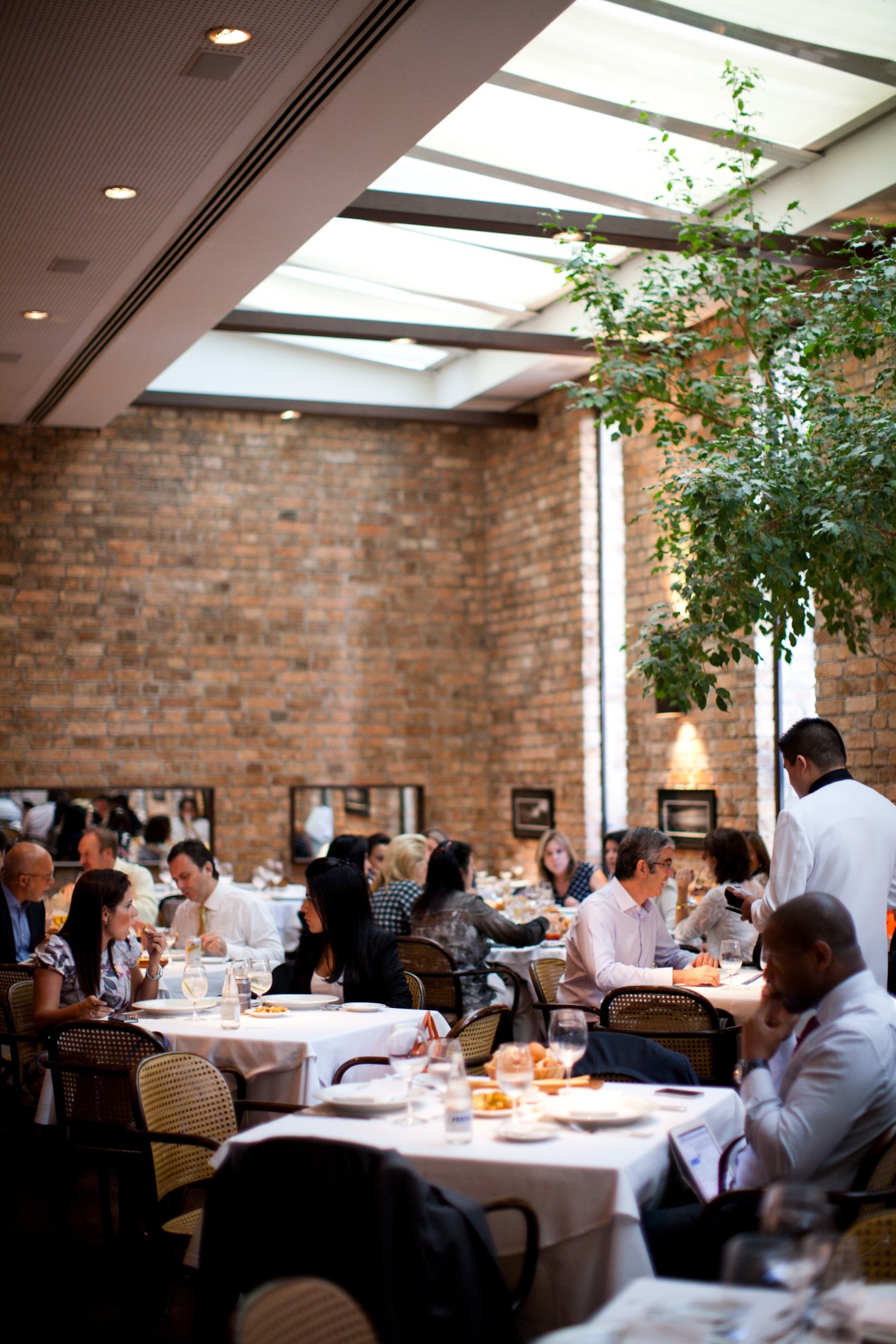 Gero restaurant dining room with brick walls, skylights, and diners seated at tables in chairs designed by Sergio Rodrigues.