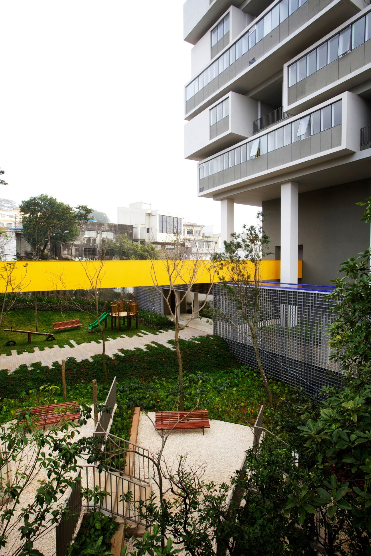 The 360º Building's ground level courtyard with play area, bench seating, and yellow boundary wall.