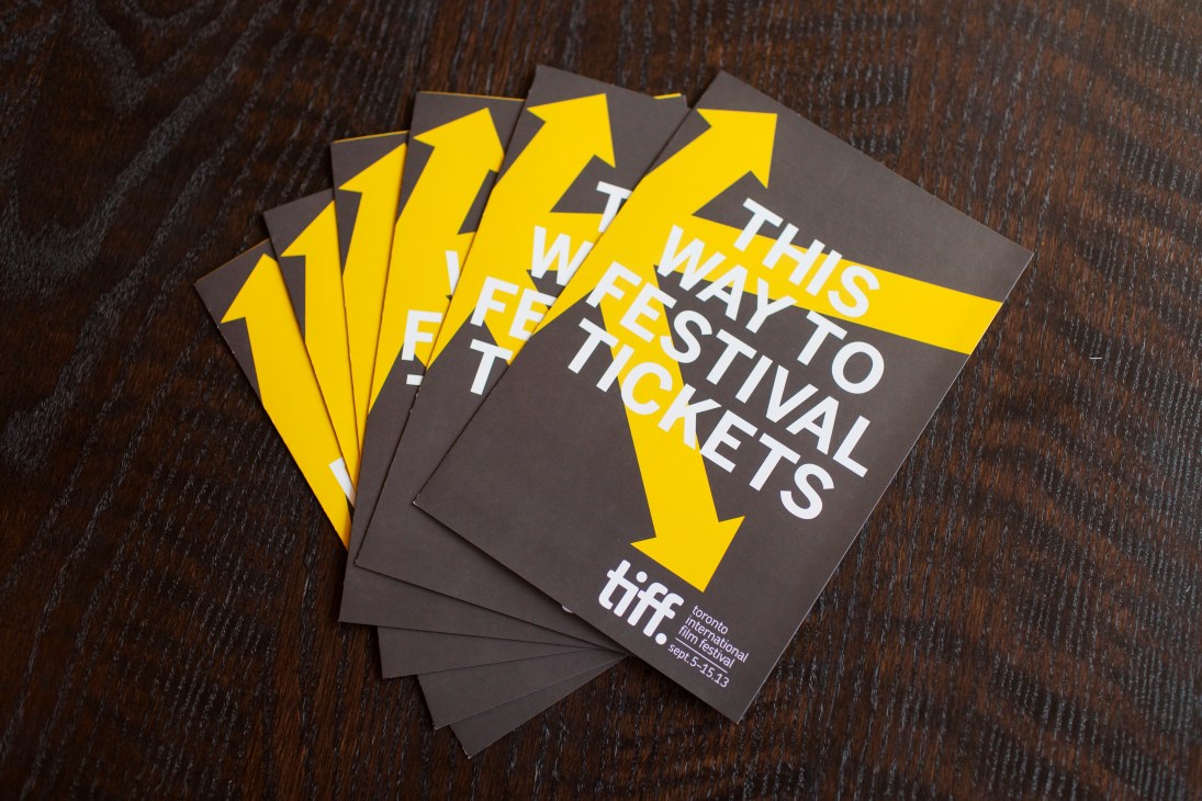 TIFF 2013 festival brochures with yellow arrows and white text on dark covers arranged on wooden surface.