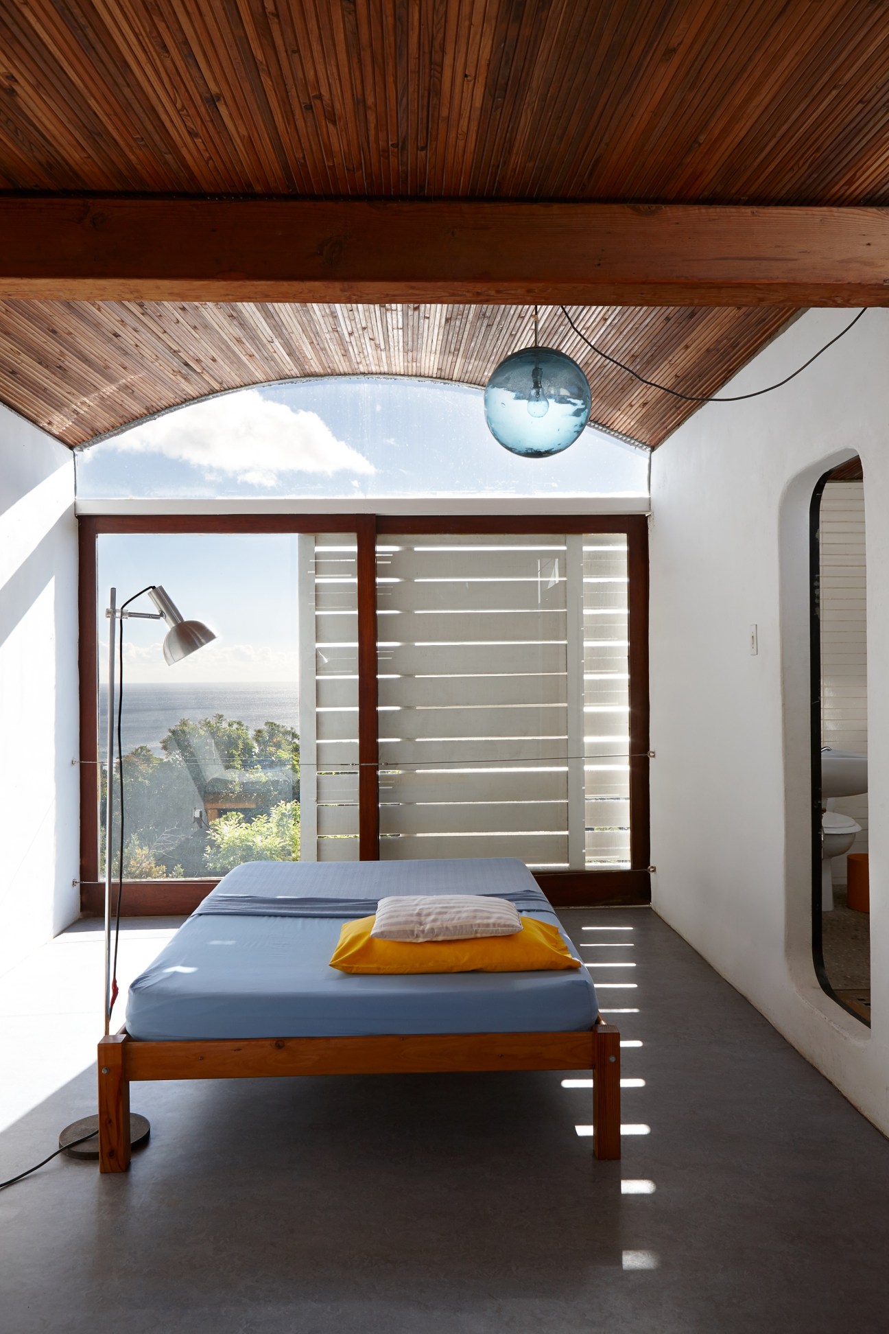 Master bedroom with wooden ceiling, ocean view through glass doors, and bed facing the Atlantic.