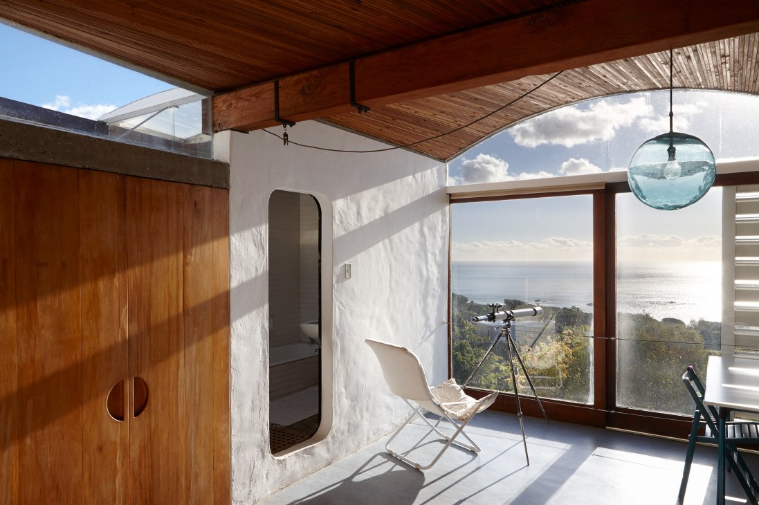 Master bedroom with wooden ceiling, white walls, and large windows overlooking the Atlantic Ocean in Die Es house.