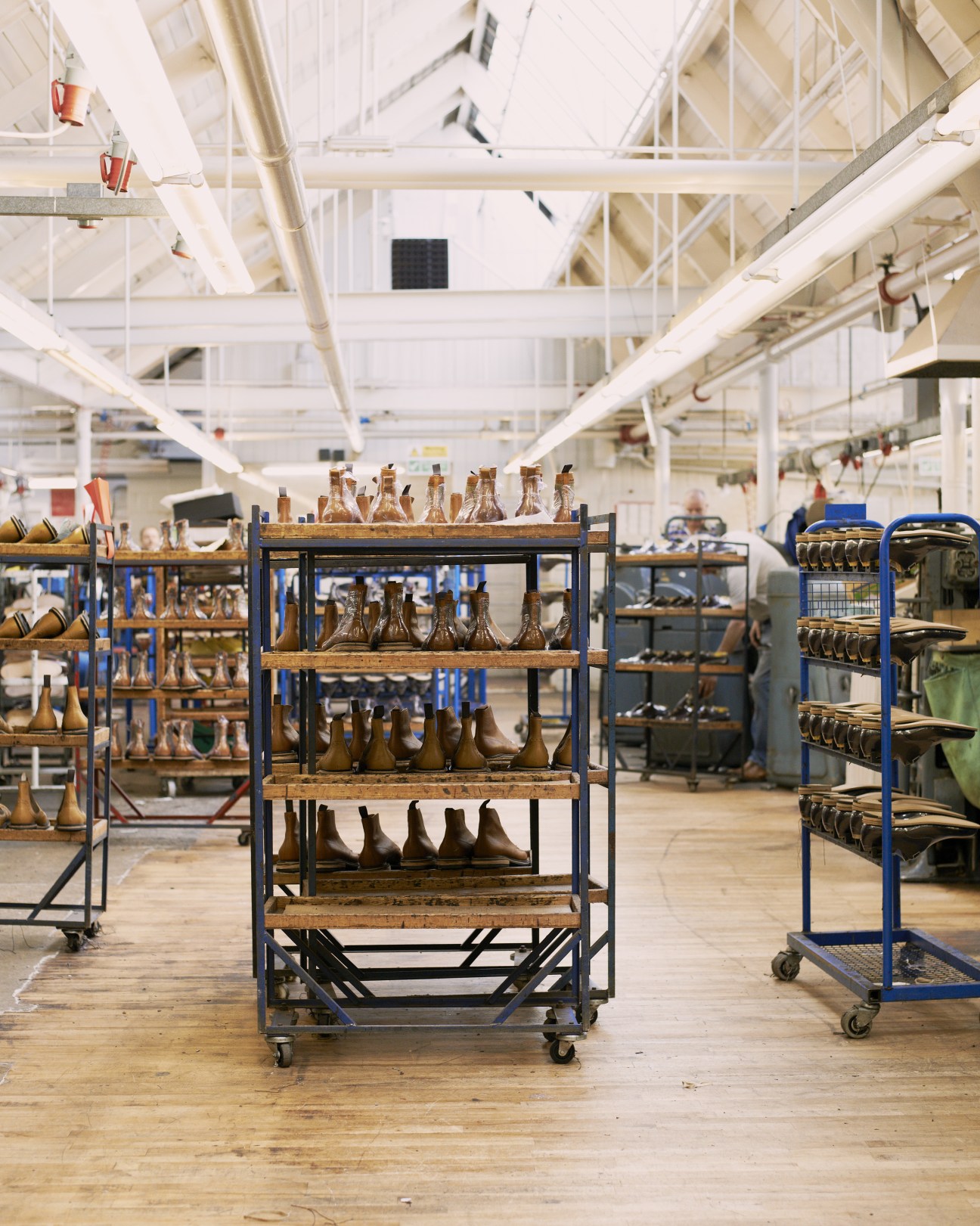 Shoe lasts displayed on metal shelving racks in a bright factory workspace.
