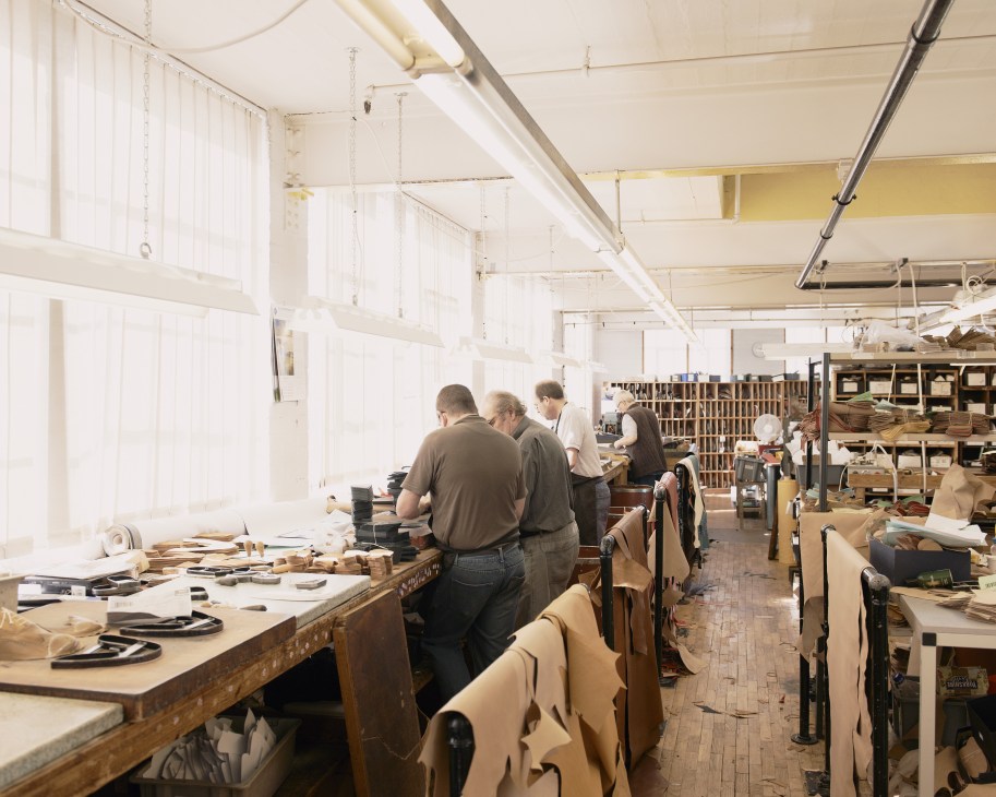 Workers in a bright factory room cutting calf leather at Joseph Cheaney & Sons shoemaking facility.