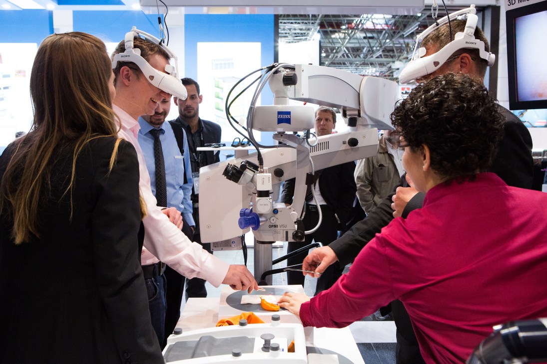 Visitors at Medica trade fair examining Sony's white 3D surgical display headset with ZEISS branding at an exhibition booth.
