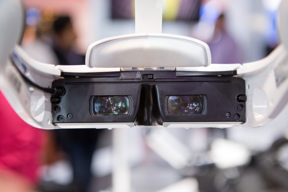 Head-mounted 3D display device with white headband and black dual lens viewer for surgical use.