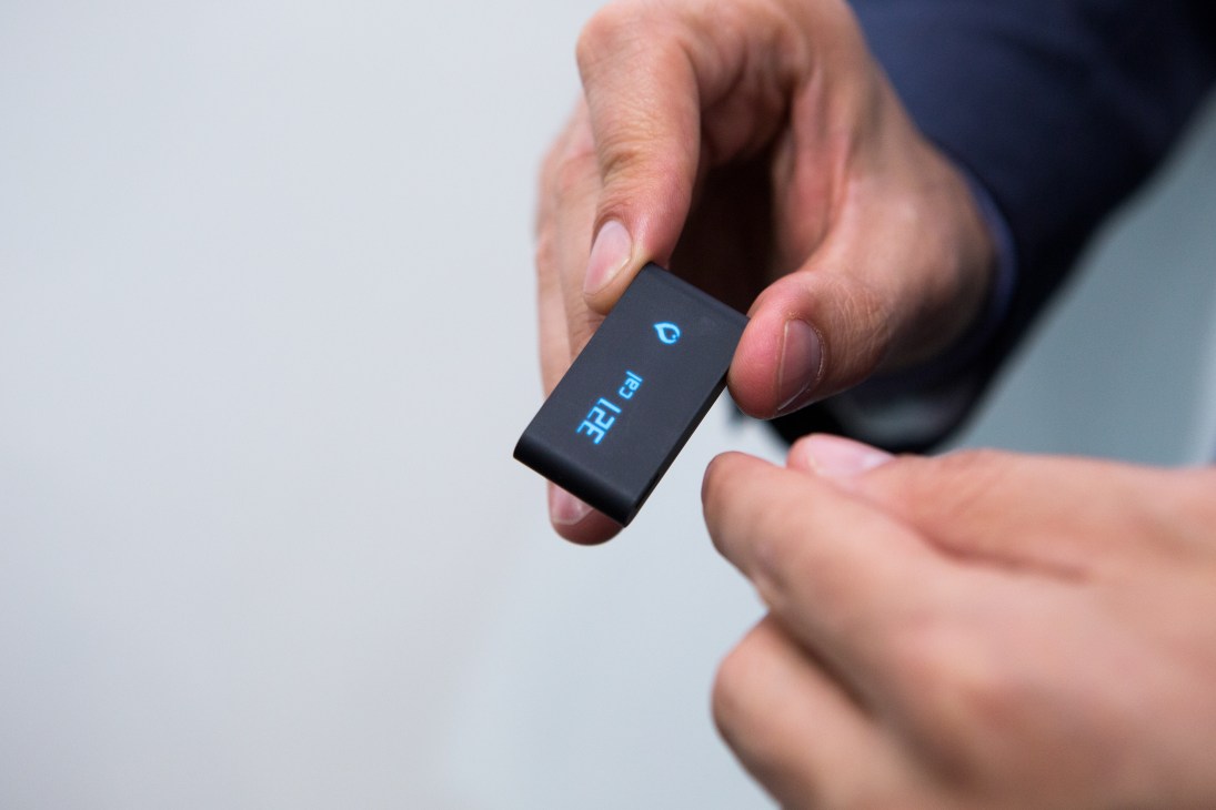 Hand holding a small black rectangular wearable device displaying 'Pulse 02' by Withings.