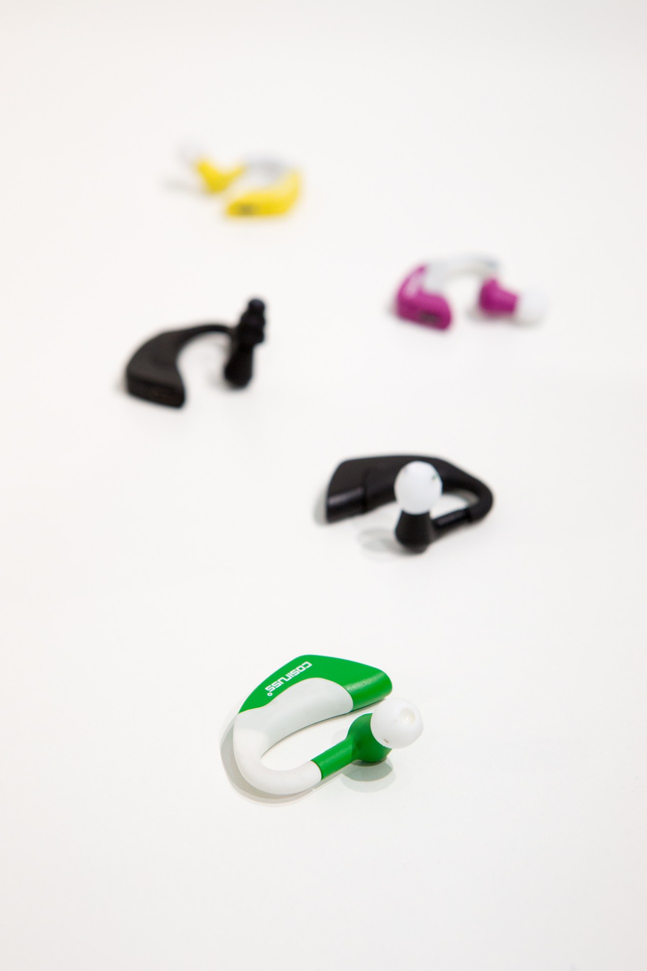 Cosinuss in-ear wearable devices in yellow, pink, black and green colors designed to monitor heart rate and temperature.