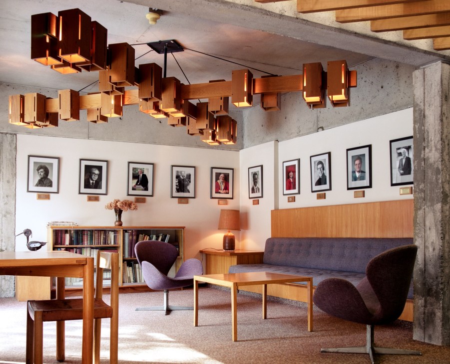Lady Eaton College's senior common room with wooden furniture, portrait gallery, and sculptural ceiling fixtures.