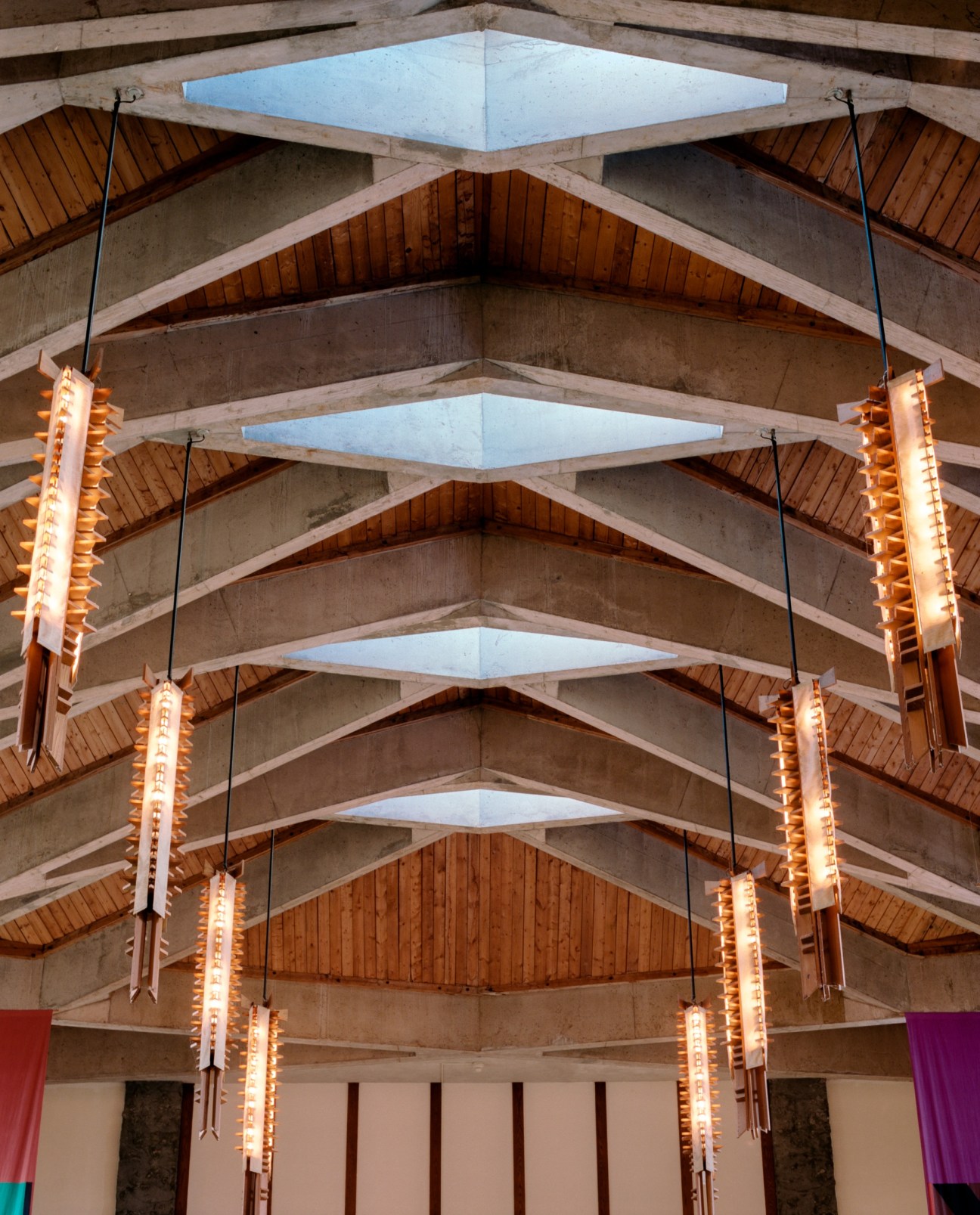 Champlain College Great Hall ceiling featuring wooden chandeliers and concrete beams with skylights.