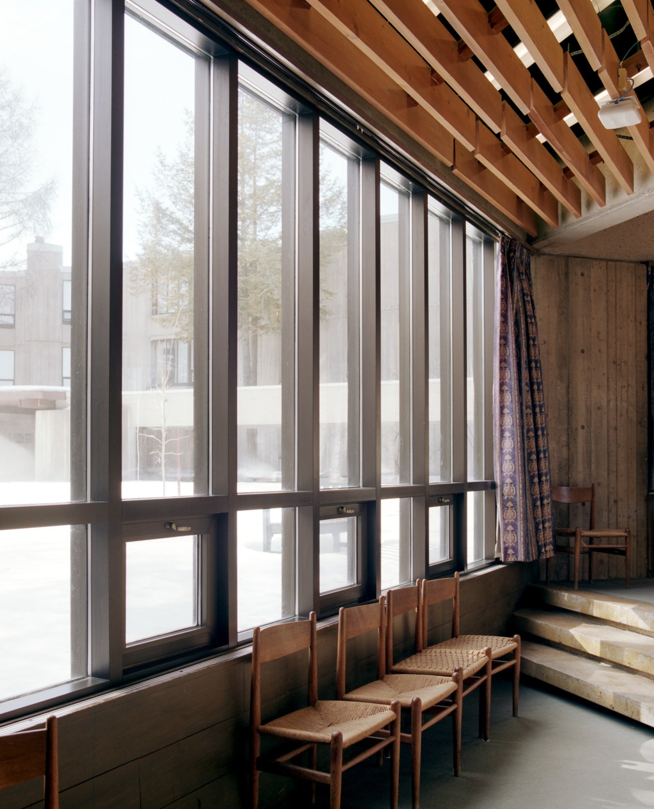 Hans Wegner chairs beside large windows with wooden ceiling beams in Lady Eaton College's interior space.
