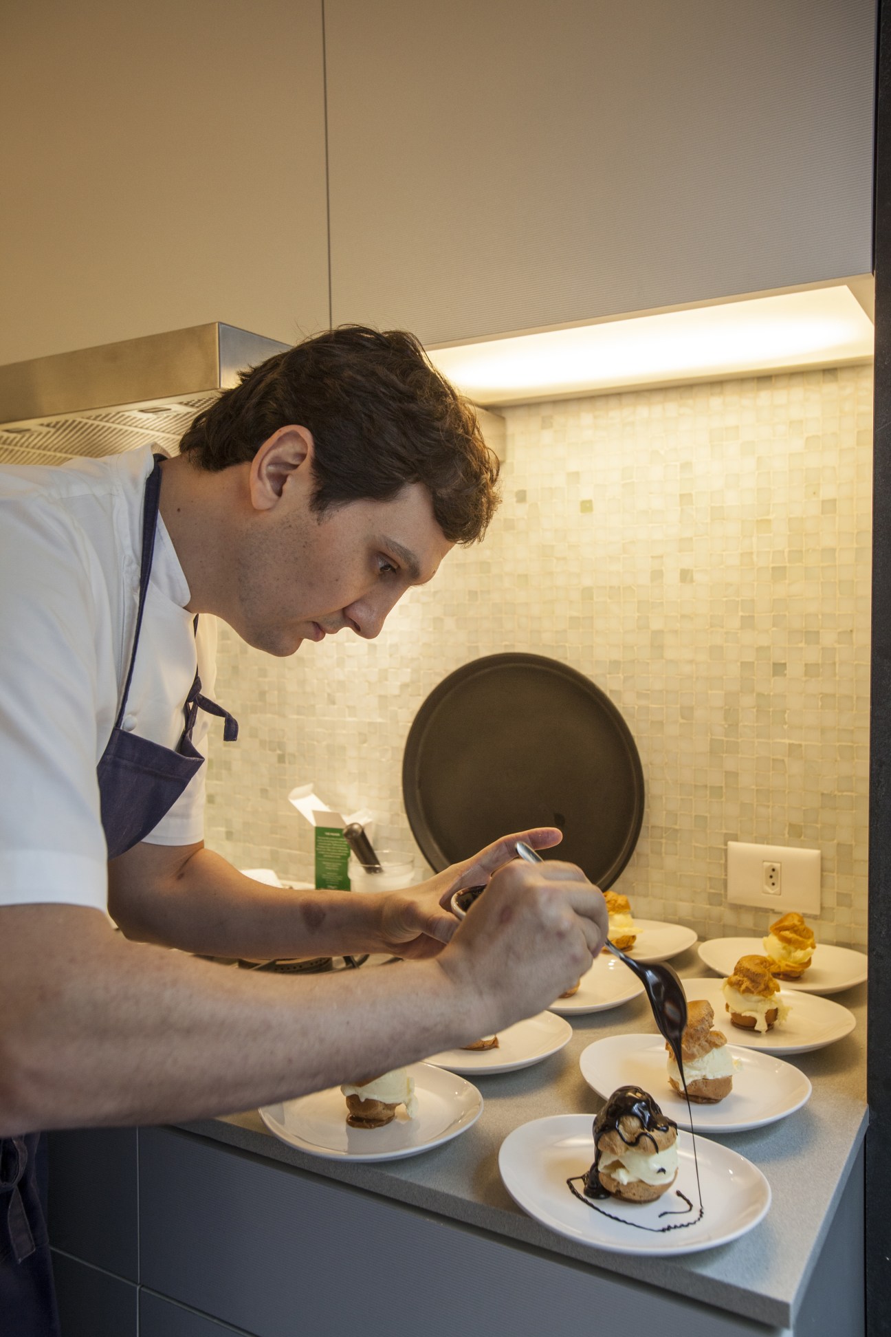 Chef Luciano Nardelli adds final touches to plated profiteroles desserts in a modern kitchen.