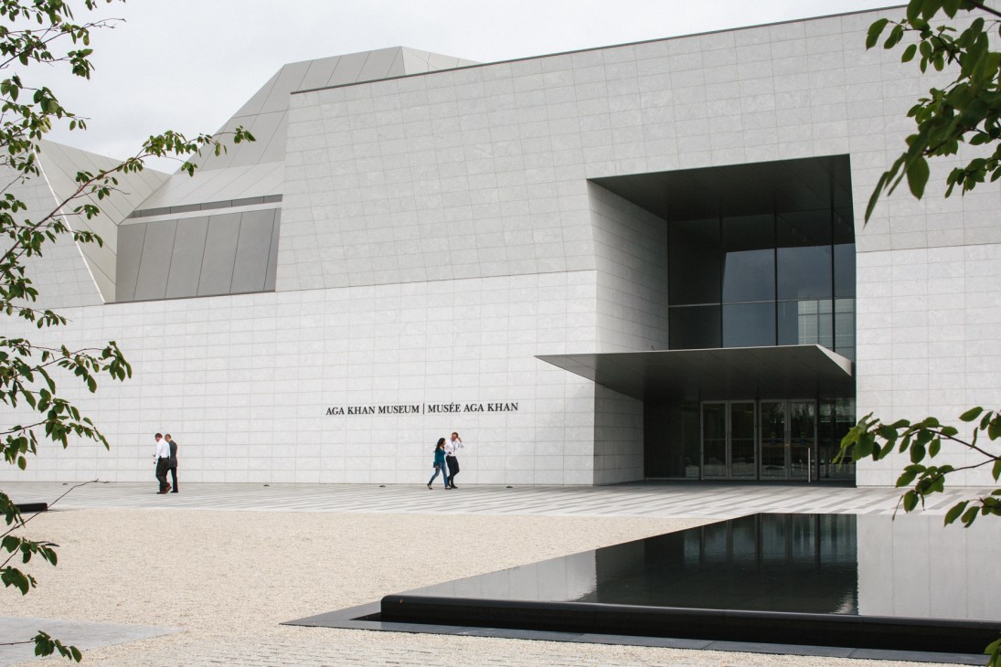 The Aga Khan Museum's white granite exterior with entrance, flanked by landscaping and reflecting pool.