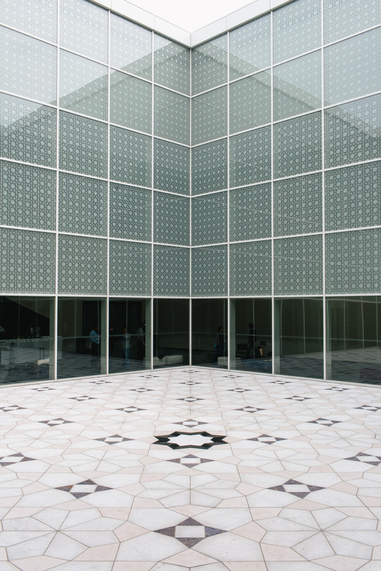 Aga Khan Museum interior courtyard with geometric mashrabiya-patterned windows and floor tiles.