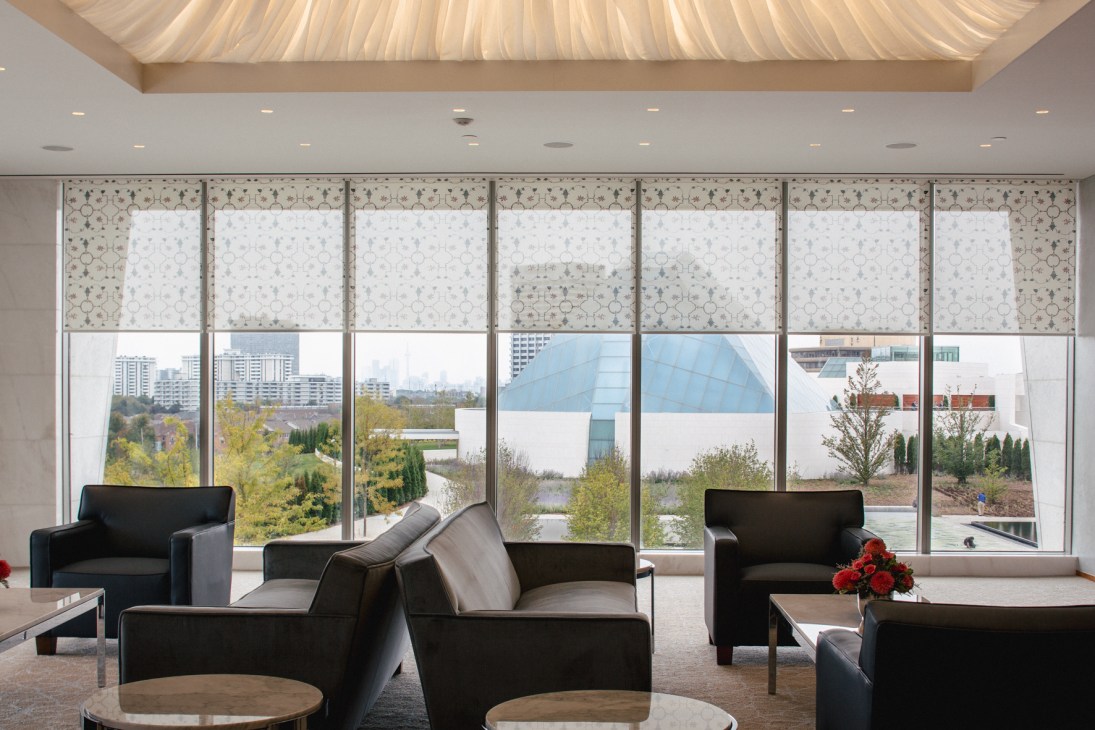 Private lounge with black seating and large windows overlooking the Ismaili Centre and garden with geometric mashrabiya patterns on glass panels.