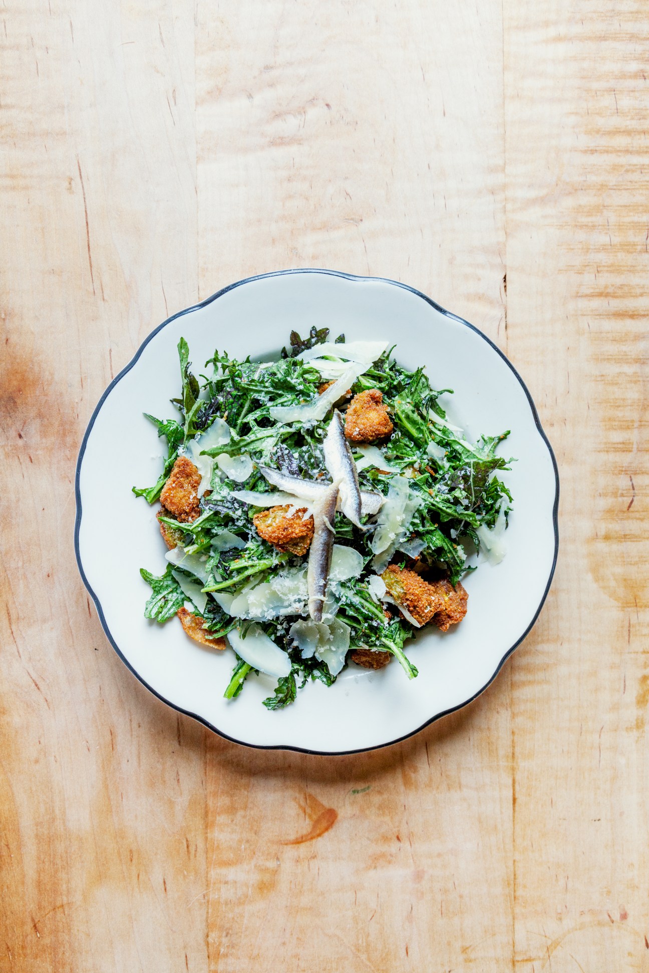 Caesar salad with crispy croutons and shaved parmesan on a white plate with blue rim.